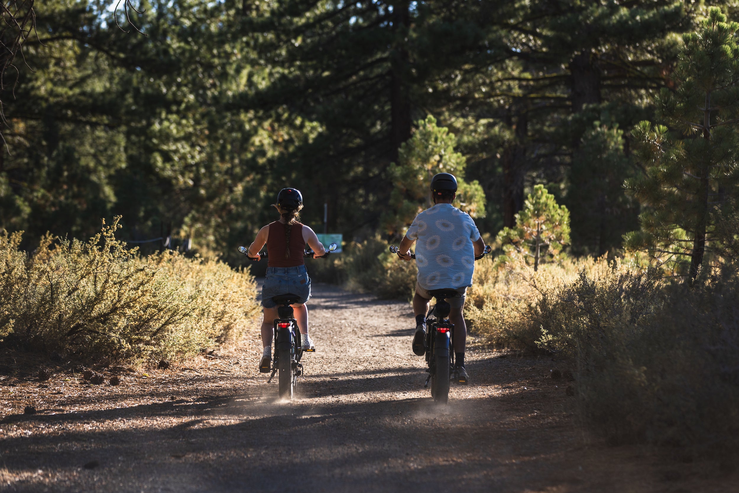 A man and woman riding the GOTRAX F3 Fat Tire Folding eBike down an off-road trail.
