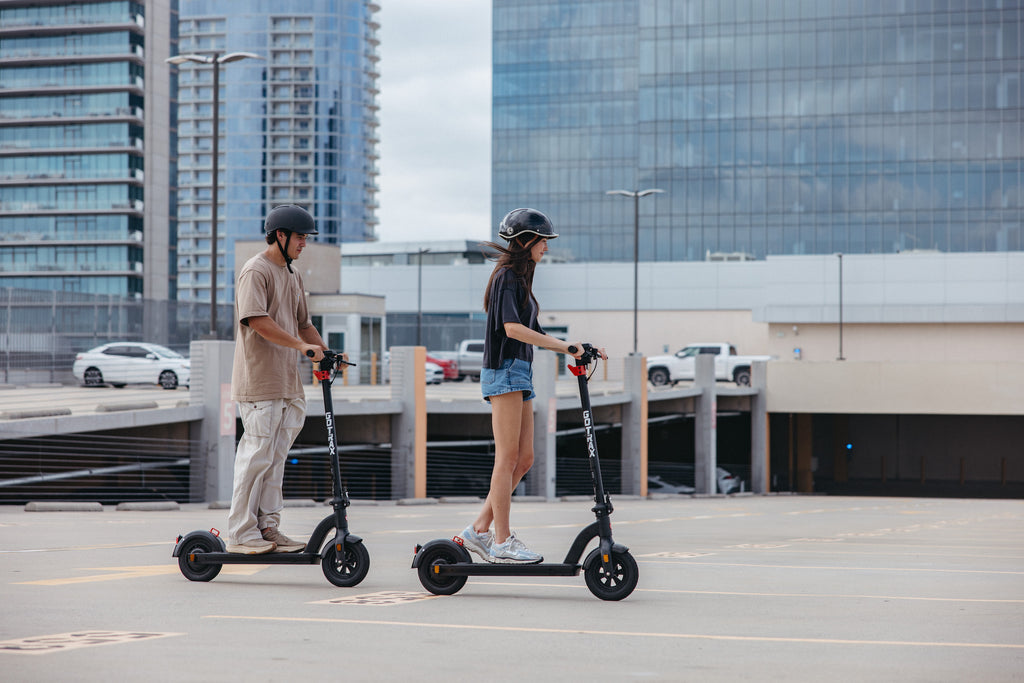 Two people riding the GOTRAX G3 Max Long Range Electric Scooter in an urban environment.