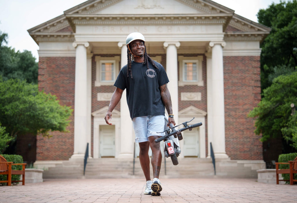 A man carrying the G5 Commuter Electric Scooter folded up down a walkway.