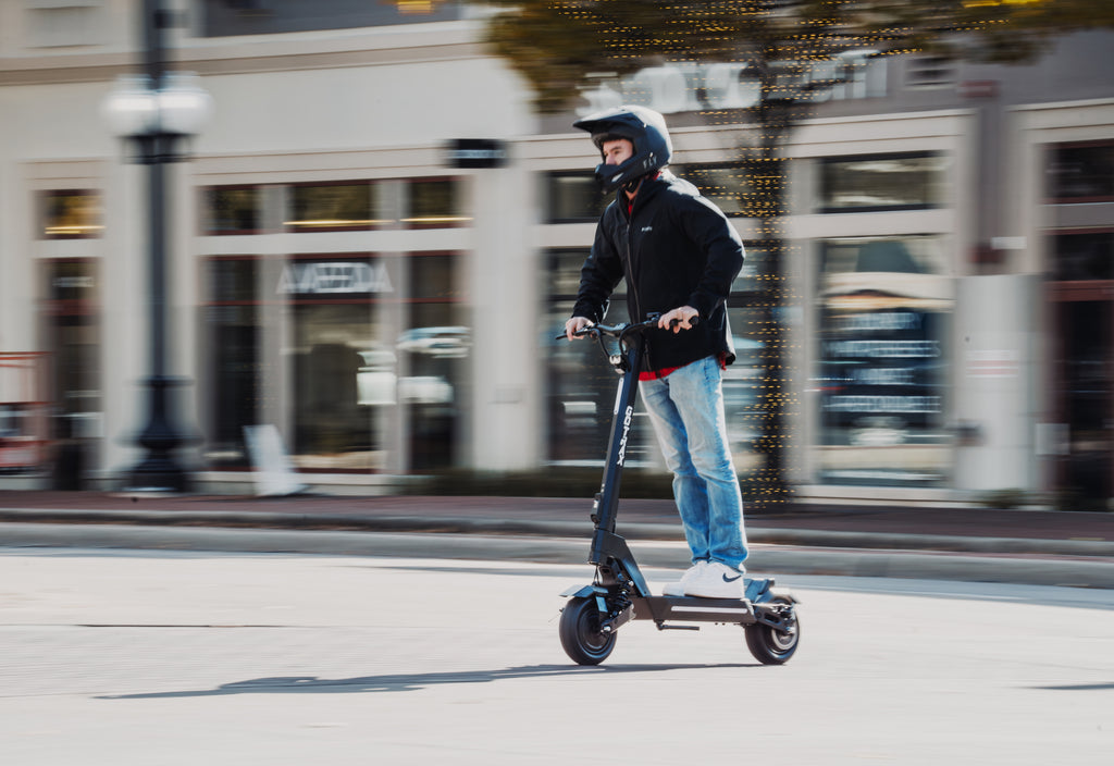 A man riding the GOTRAX GX1 Dual Motor Electric Scooter down a city street.