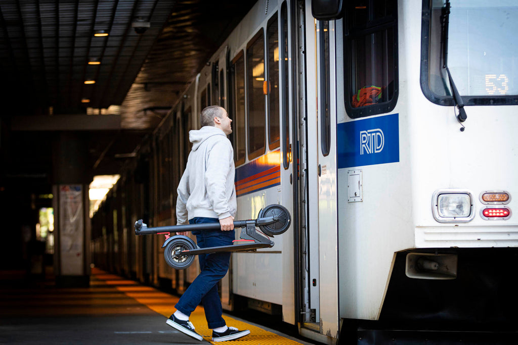 A man walking onto a bus with the GOTRAX GXL V2 Folding Electric Scooter with a lightweight frame.